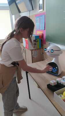 Uczniowie obserwują robota edukacyjnego. Dziewczynka rozwiązuje zadanie..jpg