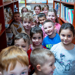 Przedszkolaki wędrują w bibliotece szkolnej pomiędzy regałami z książkami.jpg